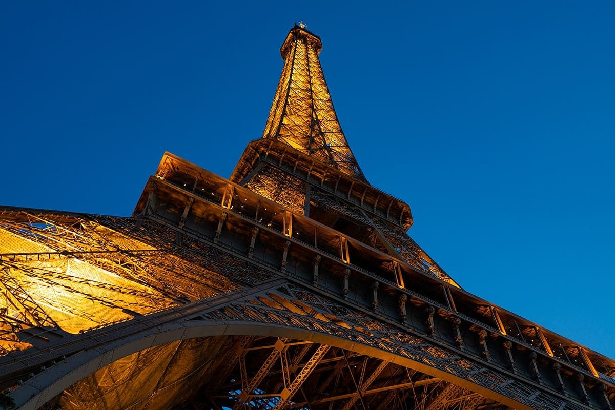 The Eiffel Tower in Paris lit at dusk, seen looking up from its base
